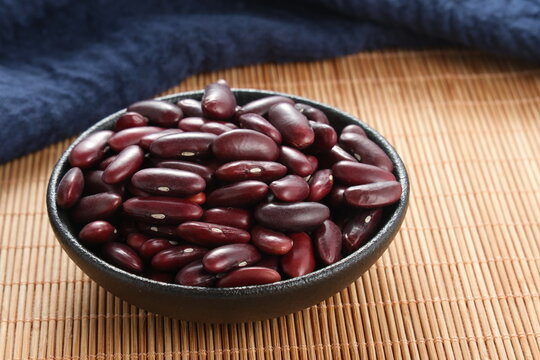 Red kidney beans in a black ceramic bowl placed on bamboo mat with navy blue fabric background