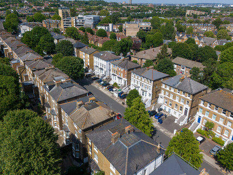 Aerial view of Ealing residential streets with rows of Victorian houses, lush green trees, and parked cars in London Borough of Ealing, England, United Kingdom.