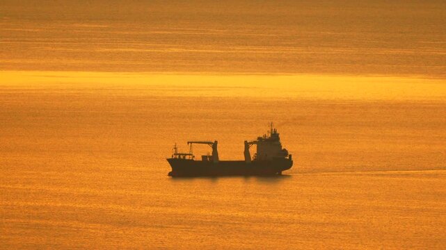 Ship sunset cargo freighter sailing across golden ocean water horizon during beautiful morning sunrise