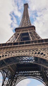 The top of the Eiffel Tower reaching into the blue sky with white clouds
