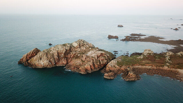 Aerial view of Pointe de Primel featuring rugged rocky cliffs and coastal formations surrounded by the Atlantic Ocean in Plougasnou, Bretagne, France.