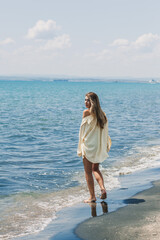 Woman walks along the shore by the blue ocean in a sunny location during the day with a light breeze and clouds in the sky © DSMT