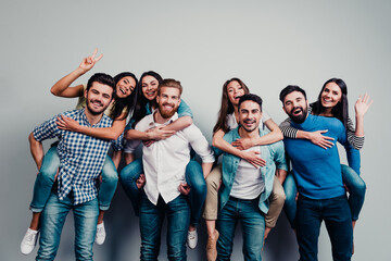 Fototapeta premium Happy group of friends enjoying piggyback rides and laughing together in casual clothing, young adults having fun and celebrating friendship in a studio portrait