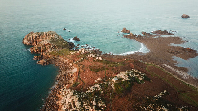 Aerial view of Pointe de Primel featuring rugged rocky cliffs, coastal paths, and a small building overlooking the Atlantic Ocean in Plougasnou, Bretagne, France.