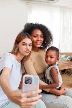 Happy close friends with little child hugging, take a photo. African curly hair woman with boy son and best friend using mobile phone to take selfies.  Lesbian couple with adopted kid, LGBT family.