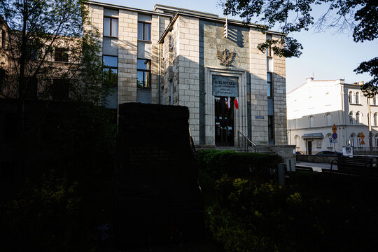 University library building with stone facade and flags at the entrance in Katowice, Poland, historic architecture and city monument framed by trees and evening light
