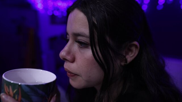 Intimate close-up shot of a woman enjoying a hot beverage in a cozy space illuminated by purple string lights, soft focus and moody nighttime ambiance, cinematic detail.