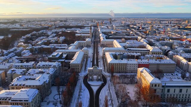 Winter drone view over Victory Gate Munich with snowy rooftops, university campus and historic boulevard. Beautiful aerial panorama of Bavaria.