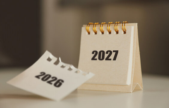 Turning the page from 2026 to 2027 &ndash; New Year calendar concept with hand and desk flip calendar	
