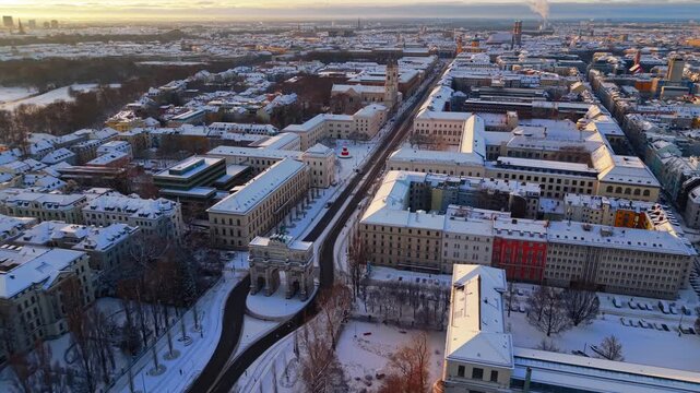 Drone footage of LMU Munich and Victory Gate in fresh snow, showing the historic boulevard, winter sunrise colors and peaceful Maxvorstadt urban panorama