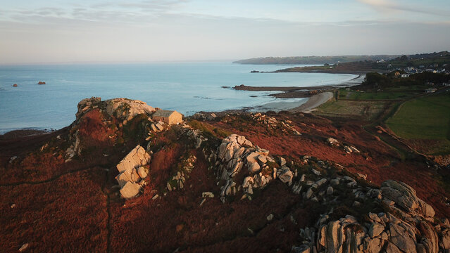 Aerial view of the Pointe de Primel headland featuring a small stone building perched on rugged granite rocks overlooking the Atlantic Ocean in Plougasnou, Bretagne, France.