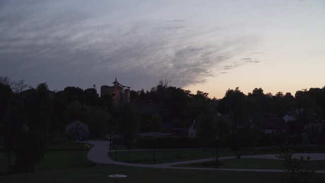 An illuminated historic castle tower stands against a cloudy twilight sky in a static wide view. Ideal for travel vlogs, historical documentaries, and evening transitions. 