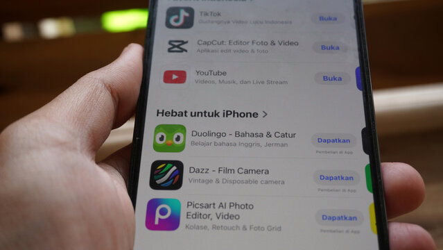 Purwokerto, Indonesia - 17 June 2026: Hand holding an iPhone browsing App Store recommendations including Duolingo, Dazz, and Picsart.
