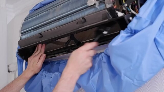Professional handyman cleaning the dirty fan turbine of a split air conditioner with a brush