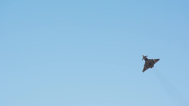 Military combat aircraft climbing away high against clear blue sky in slow motion, delta wing warplane ascending after takeoff, fighter jet gaining altitude in flight