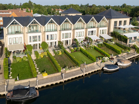 Aerial view of luxury riverside homes with manicured lawns, private boat moorings, and modern architecture along the river Thames in Maidenhead, England, United Kingdom.