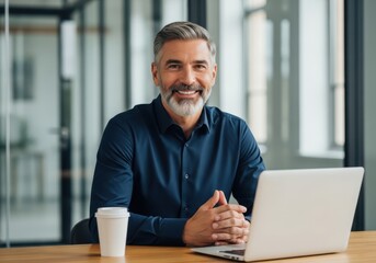 Obraz premium Smiling mature businessman sitting at desk with laptop