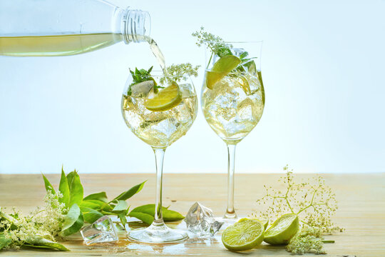 Refreshing summer drink called Hugo Spritz is poured in two wine glasses, cocktail from prosecco, elderflower, syrup, soda, mint and lemon slices, light background, copy space