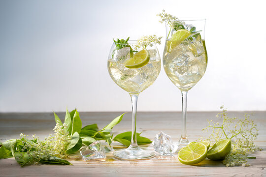Refreshing iced summer drink in two wine glasses with Prosecco, elderflower, syrup, soda, mint and lemon slices, the cocktail is called Hugo, light background, copy space
