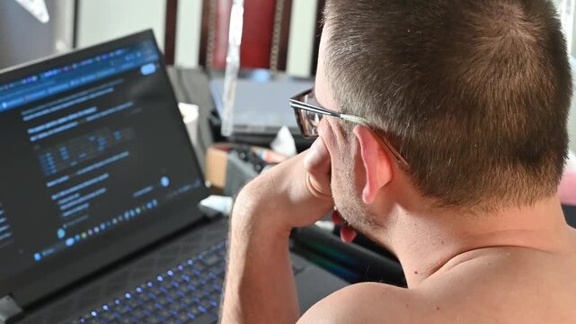Shirtless Man Working on a Computer at Home During Hot Weather