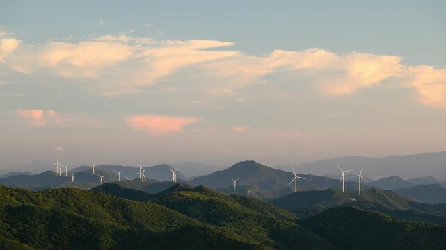Timelapse of a Wind Turbine Farm on a Forested Mountain Ridge at Sunset. Wind turbines generate clean renewable energy.	
