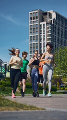 Obraz premium Group of young friends jogging together through modern city park during outdoor fitness workout. Concept of healthy lifestyle, active recreation, cardio exercise, teamwork and urban wellness.