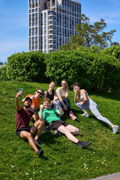 Friends taking selfie on grass after outdoor running workout. Concept of fitness recovery, social media content, running club friendship, healthy lifestyle, outdoor recreation and community wellness.