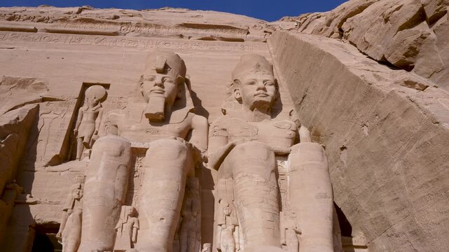 Low angle view of the massive stone statues of Ramses II at the ancient Abu Simbel Temple in Aswan, Egypt, featuring intricate carvings and hieroglyphs.