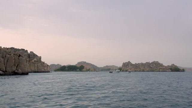 A scenic view of the ancient Philae Temple complex on Agilkia Island in Aswan, Egypt, seen from a small boat on the Nile River.