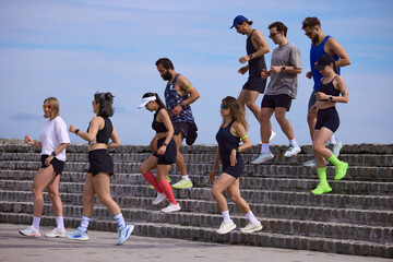 Fototapeta premium Mixed running club going down stone steps after outdoor training session. Concept of recovery pace, team fitness, urban cardio, endurance practice and healthy active lifestyle.