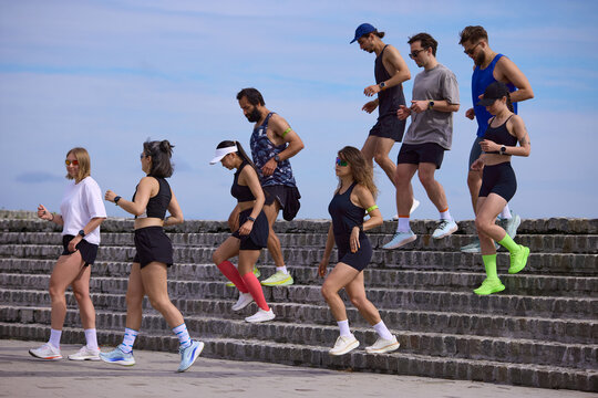 Mixed running club going down stone steps after outdoor training session. Concept of recovery pace, team fitness, urban cardio, endurance practice and healthy active lifestyle.