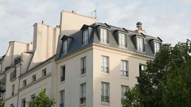 Low-angle architectural view of a classic Parisian Haussmann building corner, showing typical cream stone facades, wrought iron balconies, and a zinc mansard roof camera tilting slowly up