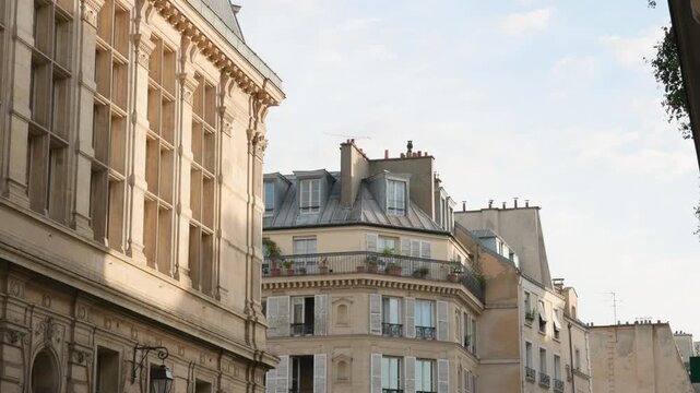 Architectural view of historical Parisian street buildings featuring detailed stone facades, window shutters, and a zinc mansard roof under a bright sky.