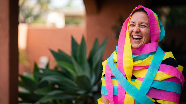 Hispanic woman wrapped in colorful paper streamers laughing. Joyful person celebrating during a traditional Mexican holiday party. Festive concept of happiness, fun and cultural event.