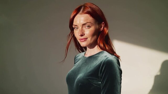 Posing adult female model making turns while gust lifts red hair in studio, teal velvet, shadow
