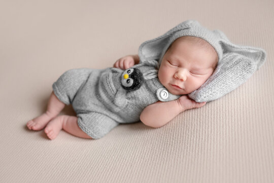 Infant sleeps softly. Wears gray knitted penguin themed romper. Professional newborn photoshoot.
