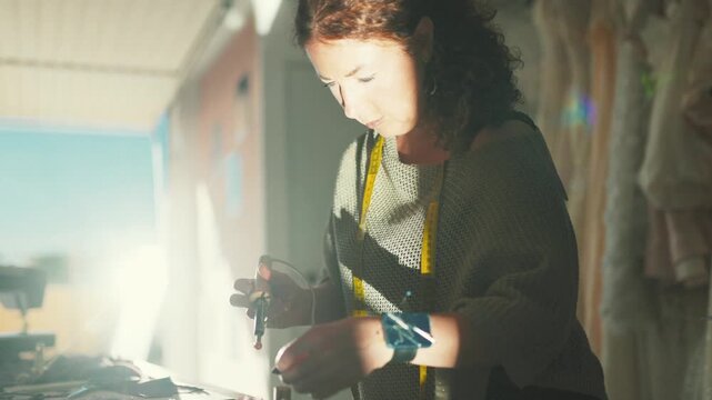 Fashion designer works on a dress in bright workshop with sewing tools and materials during afternoon hours