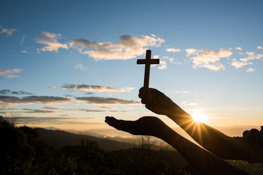 jesus on the cross. Silhouette of Hand hold cross of God. Silhouette of a man holding a cross at sunset in contemplation. The hands of Jesus resurrected from the tomb and bright light background,