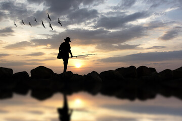 Silhouette of man fishing rod sunset and birds background. man with a fishing rod in the lake at sunset/man stands with a fishing rod on the lake at sunset.  © Luis