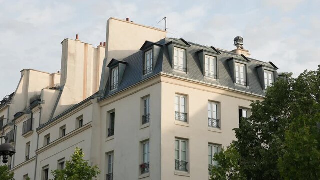 Low-angle architectural view of a classic Parisian Haussmann building corner, showing typical cream stone facades, wrought iron balconies, and a zinc mansard roof with dormer windows.