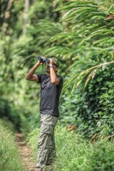 Fototapeta premium Nature lover exploring a lush tropical forest with binoculars in the Western Ghats of Munnar, India, embracing eco-tourism and adventure