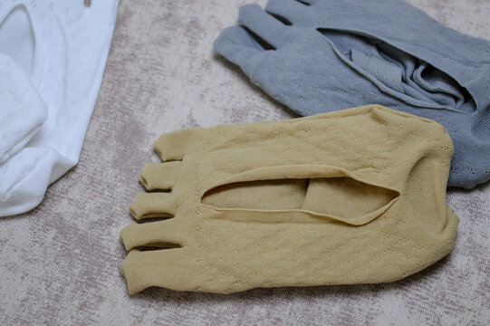 beige, white, and grey toe socks on a textured fabric. This five-finger design promotes natural toe alignment, enhancing foot health, hygiene, and comfort for barefoot footwear users.