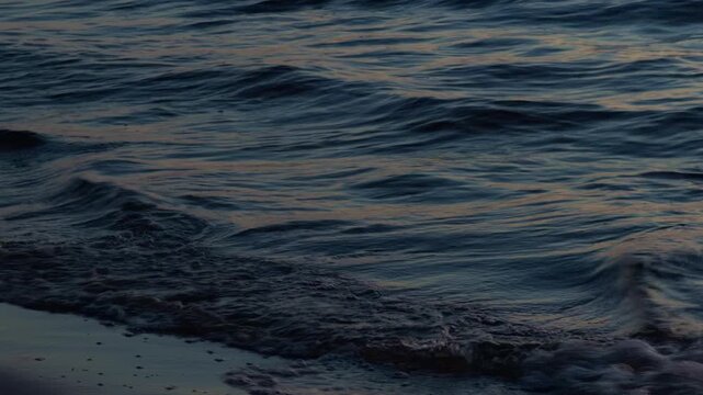Dark ocean waves rolling onto quiet shoreline at dusk with soft reflections and gentle surf