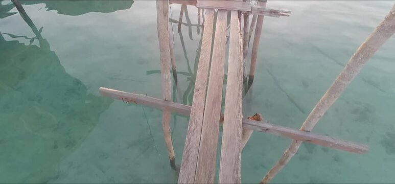 a serene and immersive visual journey across a rustic, handmade wooden footbridge. Suspended just over breathtakingly clear, turquoise sea water