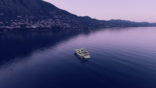 Luxury motor yacht anchored near Verga coastline at dawn, calm Mediterranean sea, mountain village and coastal cliffs near Kalamata, Greece
