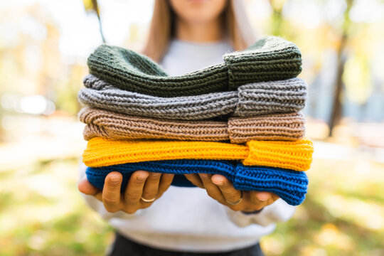 Woman holding a stack of colorful knitted beanie hats in her hands outdoors.