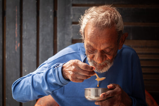 Indian senior man tasting soup from a metal bowl