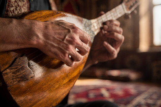 A close-up photo of a musician's hands playing a traditional wooden stringed instrument (saz or baglama)