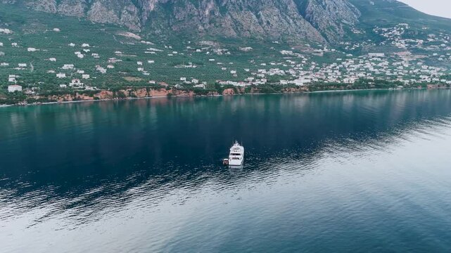 Anchored motor yacht near Verga coast, aerial view of calm Mediterranean sea, mountain village and coastal cliffs near Kalamata, Greece