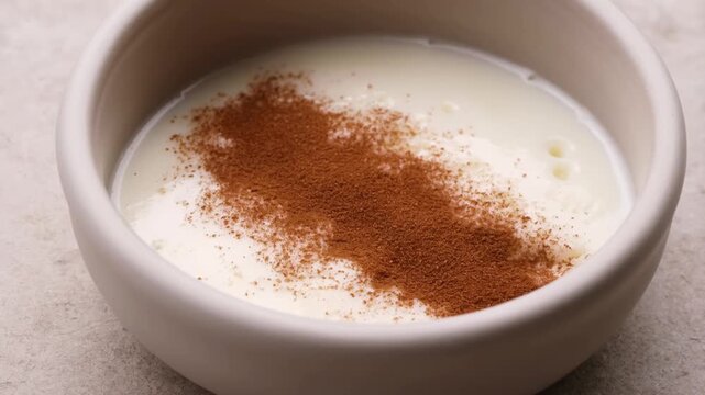 A close-up video captures a bowl of creamy white rice pudding, beautifully garnished with a line of cinnamon powder, emphasizing its smooth texture and appetizing presentation.